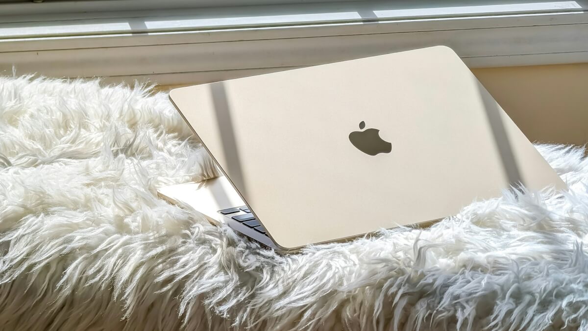 an apple laptop sitting on a fluffy blanket in front of a window