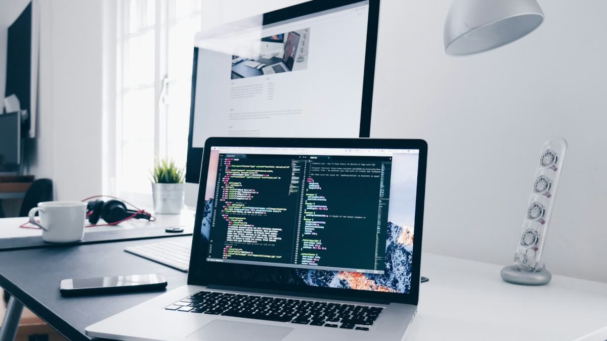 A MacBook with lines of code on its screen on a busy desk