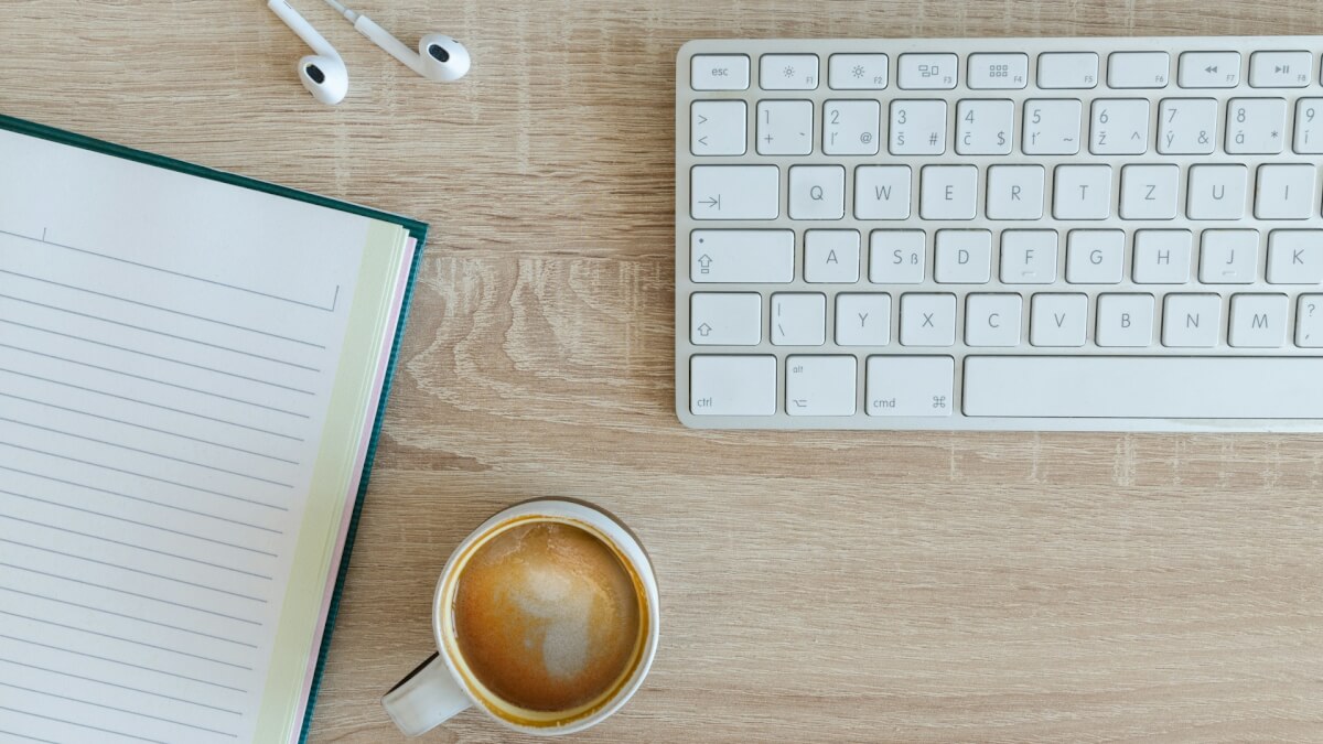 coffee latte near white wireless keyboard and Apple EarPods on the table photography