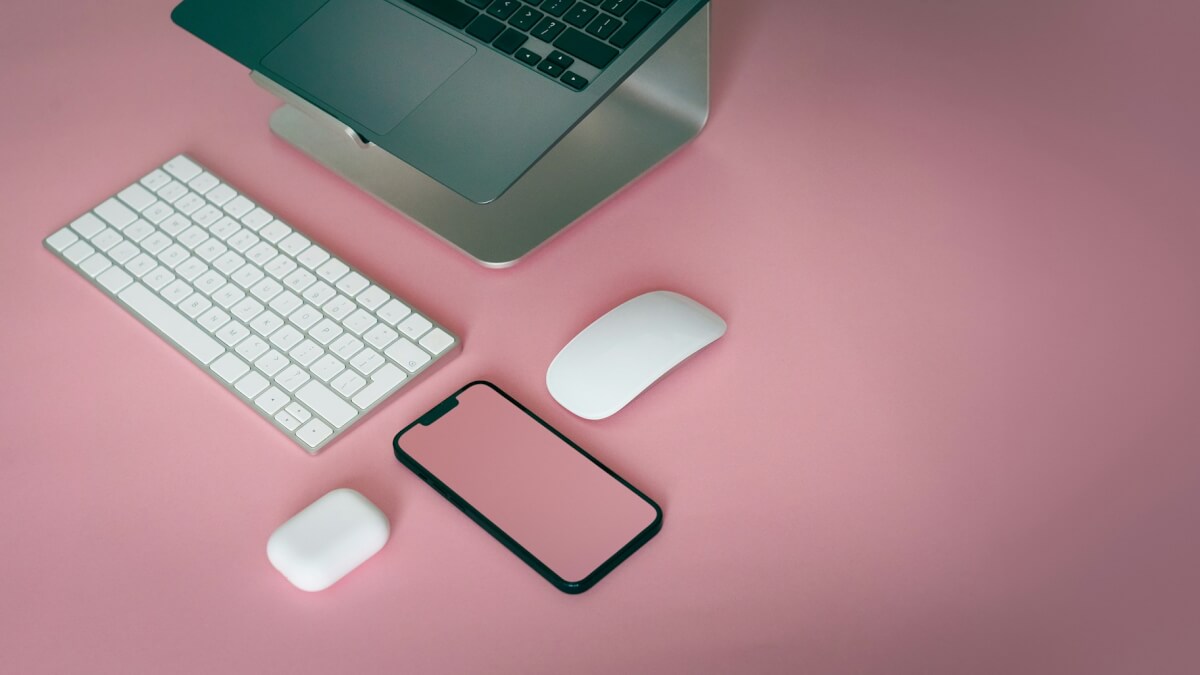 a computer keyboard, mouse, and cell phone on a pink surface